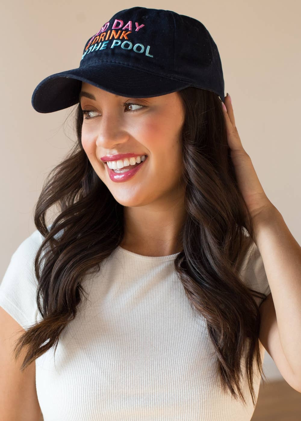 Woman wearing a navy blue cap with colorful text, smiling against a neutral background